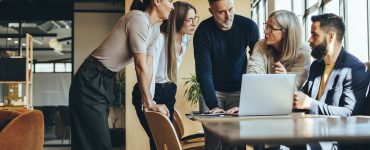 People in an office standing around a table discussing talent acquisition